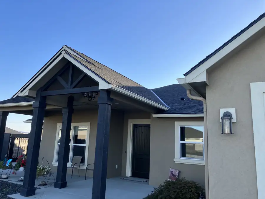 Finished dark-shingle roof on a grey stucco home with a timber-post gabled porch
