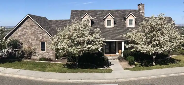 Stone-front home with three dormers under a new roof and flowering trees