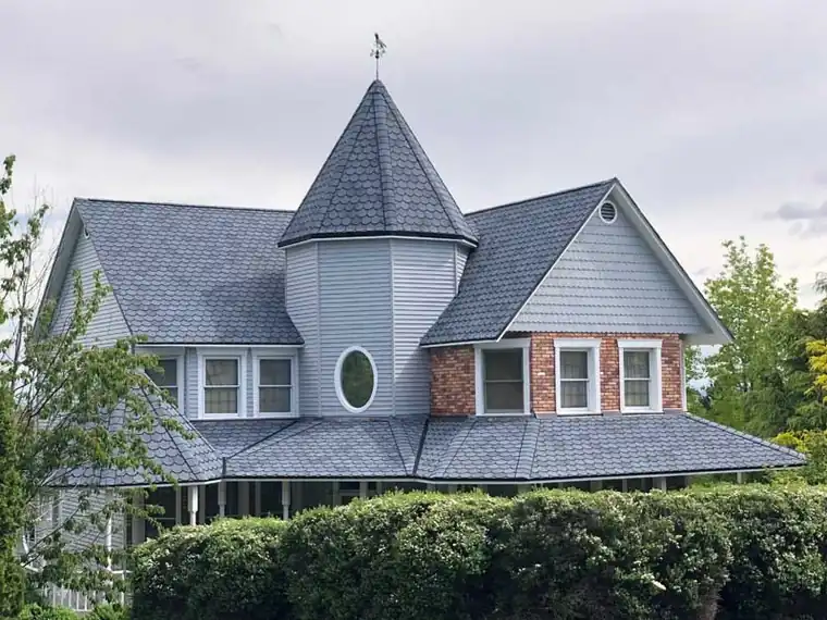 Victorian home with a turret and wraparound porch under a new dark shingle roof