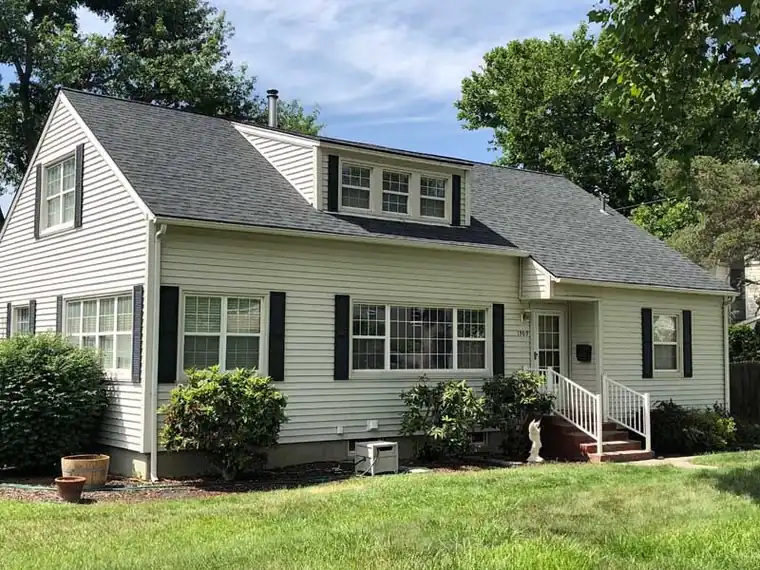 Cream Cape Cod home with a dormer under a new dark shingle roof