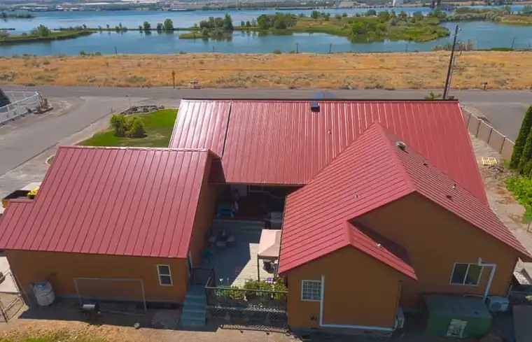 Drone view of a red standing-seam metal roof on a home near the water
