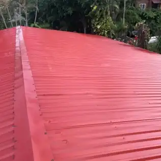 Red corrugated roof panels going on over the open frame in Honduras